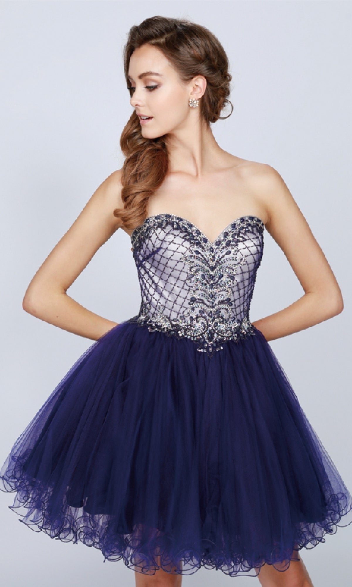 A woman models the Juliet 778 Short Babydoll Hoco Dress, featuring a strapless sweetheart neckline, beaded bodice, fitted top, and short dark blue tulle skirt, against a plain background.